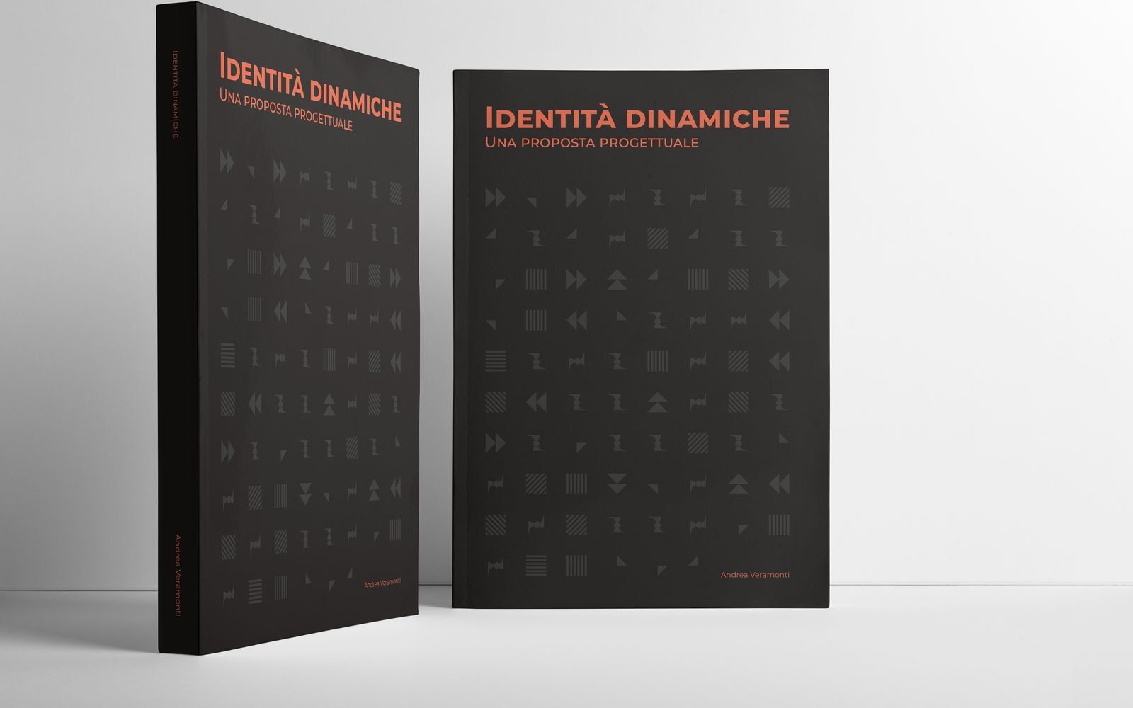 Due copie del libro Identita' dinamiche in piedi su un fondo grigio chiaro, una di tre quarti col dorso a vista e una di fronte: copertina nera, il titolo in arancione con sotto Una proposta progettuale, una trama di elementi geometrici grigi su tutta la superficie e il nome Andrea Veramonti in basso a destra.